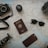 A collection of travel-related items is arranged on a map. Items include a camera with a strap, a lens cap, a passport, sunglasses, a knife, a smartphone, a tripod, and parts of a pair of shoes. All these objects suggest preparation for a journey.